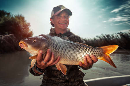 Happy young fisherman holds the big Carp fish (Cyprinus carpio) and smilesの写真素材