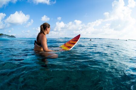 Young woman surfer sits on the surf board in the ocean in Maldives. Lady looks at the horizon and waits her waveの写真素材