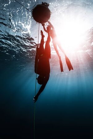 Freediver descends along the rope into the depth while another freediver relaxes on the buoy