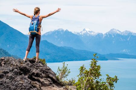 Young woman hiker stands on the rock with stretched hands and enjoys the mountains viewの写真素材