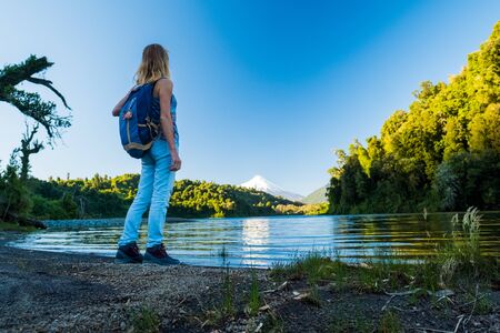 Woman stands on the coast of the blue lake with volcano of Osorno on the background. Patagonia, Chileの写真素材