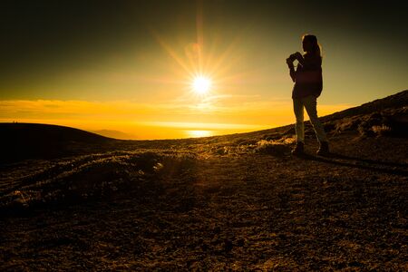 Woman photographer stands on the loose volcanic ground with sun shining behindの写真素材
