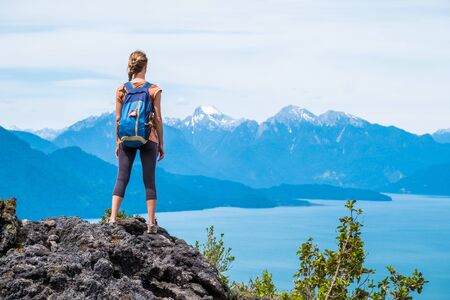 Young woman hiker stands on the rock and enjoys mountains viewの写真素材