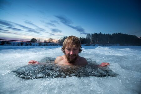 Young man with beard swims in the winter lakeの写真素材