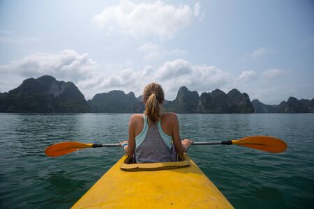 Woman sits in the yellow kayak and enjoys the Ha Long Bay view in Vietnamの写真素材
