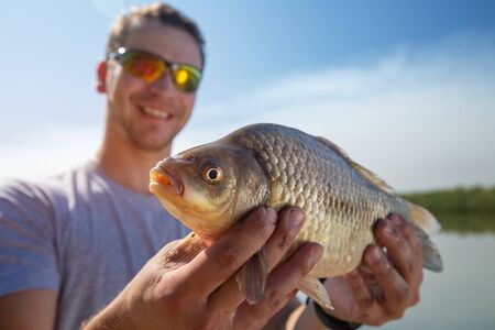 Young happy angler holds the fish (Carassius) and smilesの写真素材