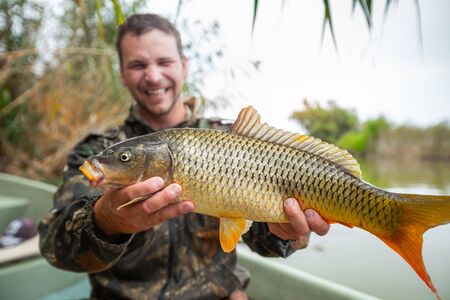 Young happy angler holds the big Carp fish (Cyprinus carpio) looks at the camera and smilesの写真素材