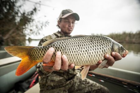 Young amateur angler holds the big Carp fish (Cyprinus carpio) being in the boat on the riverの写真素材