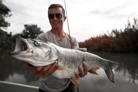 Amateur angler stands in the boat, smiles and holds the trophy Asp fish (Leuciscus aspius)の写真素材