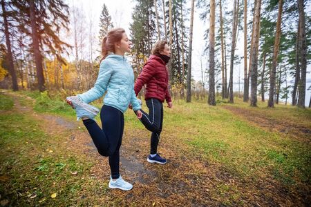 Young sportive couple doing stretching exercises in the autumn forest. Young man and woman warm up in the forestの写真素材