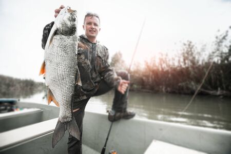 Amateur angler stands in the boat and holds the trophy Asp fish (Leuciscus aspius) with natural...