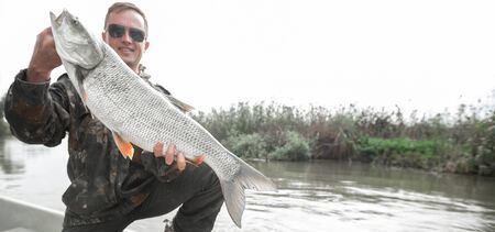 Amateur angler stands in the boat and holds the Asp fish (Leuciscus aspius) which is 4kg (8.8 lb) being on the riverの写真素材