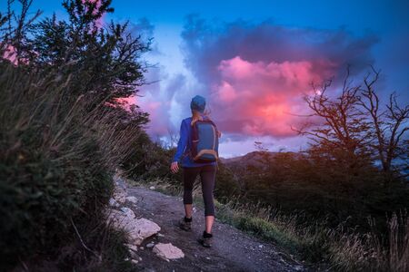 Woman hiker walks on the trail with bright pink cloud in the morning skyの写真素材