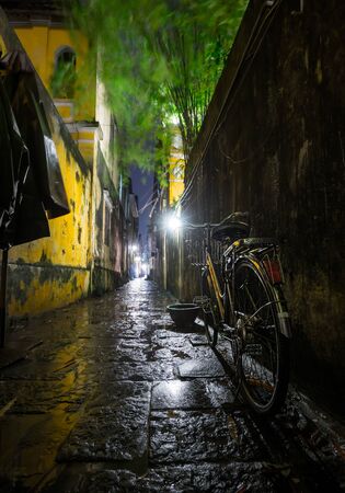Wet bicycle stands near the wall on the narrow wet street in the town of Hoi An in Vietnamの写真素材