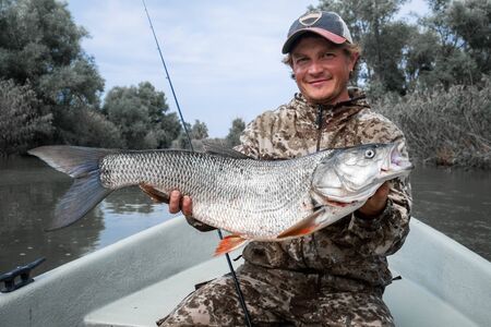 Young angler holds the trophy Asp fish (Leuciscus aspius) being in the boat on the river.の写真素材