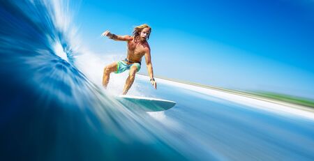 Young man surfer with long hair surfs the fast and perfect ocean wave in Maldivesの写真素材