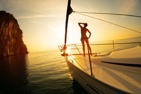 Young woman meets sunrise on the yacht anchored in the tropical seaの写真素材