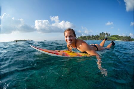 Happy woman surfer lies on the surf board in the ocean in Maldives. Girl looks at the camera and smilesの写真素材