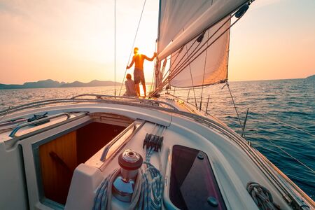 Young couple enjoys sailing in the tropical sea at sunset on their yacht.の写真素材