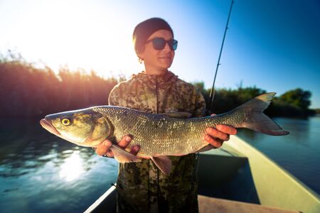 Happy fisherman holds trophy Asp fish standing in the boatの写真素材