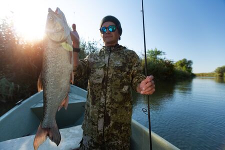Fisherman holds Asp fish standing in the boat on the riverの写真素材