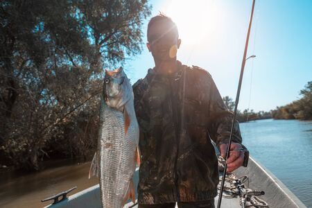 Happy fisherman holds trophy Asp fish being in the boat on a lakeの写真素材