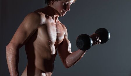 Young bodybuilder with naturally looking and wet body (body has hairs and birthmarks) holds dumbbellの写真素材