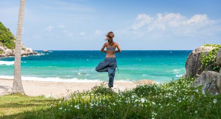 Young woman performs yoga exercises on a green lawn with sea on the backgroundの写真素材
