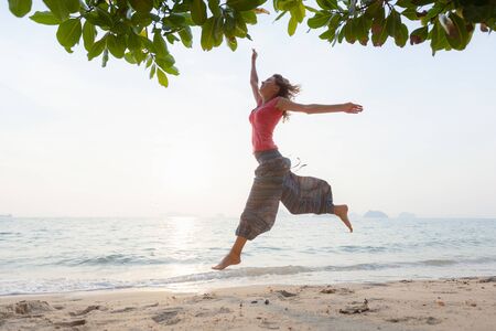 Young woman in hippie pants runs and jumps on the sandy tropical beachの写真素材