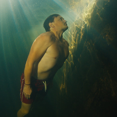 Man dives in the freshwater river with sunny rays shining through the water and swims near the rockの写真素材
