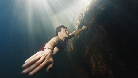 Man dives in the freshwater river with sunny rays shining through the water