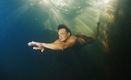 Man dives in the freshwater river with sunny rays shining through the waterの写真素材