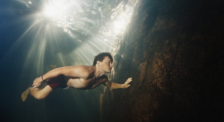 Man dives in the freshwater river with sunny rays shining through the waterの写真素材