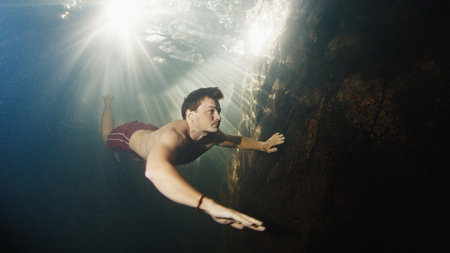 Man dives in the freshwater river with sunny rays shining through the waterの写真素材