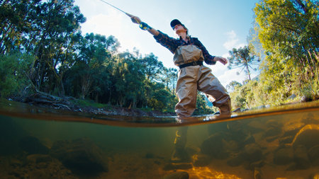 Woman angler on the river. Woman stands in the water in waders and casts the line. Woman fishing on the riverの写真素材
