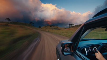Woman steers the car on a rural road at vivid sunset. Solo female traveler drives the car on an empty unpaved roadの写真素材