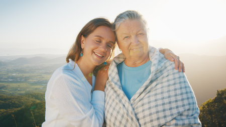 Portrait of two women young and elderly. Young woman hugs senior caucasian woman outdoor at sunrise. Models look into the cameraの写真素材