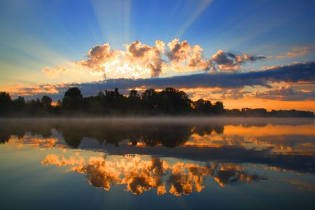 sunrise with sunbeams and clouds and reflection in riverの写真素材