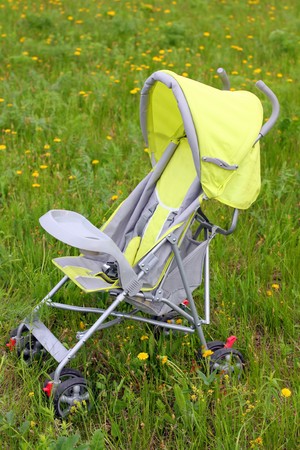 baby stroller on green lawn with blossom dandelionsの写真素材