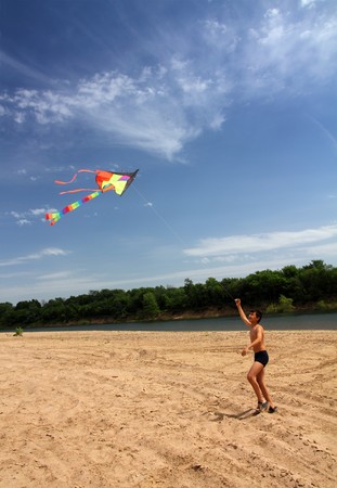 asian boy running kite on river beachの写真素材