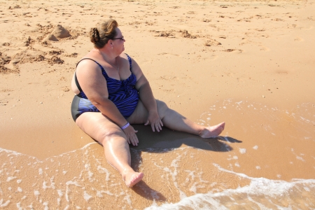 overweight woman sitting on beach near seaの写真素材