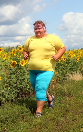 fitness - overweight woman running along field of sunflowersの写真素材