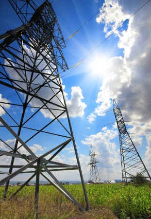 tall electric masts against sun and cloudy skyの写真素材