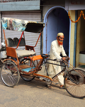 AGRA, INDIA - NOVEMBER 16, 2012: Old indian man rickshaw rolls his bike on street in Agra, India, 16 nov 2012のeditorial素材