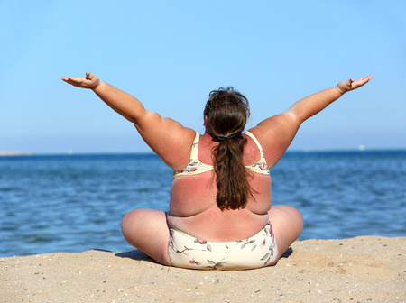 overweight woman sitting on beach with hands upの写真素材