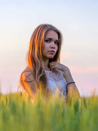 Portrait of a pretty girl in a wheat field at sunsetの写真素材