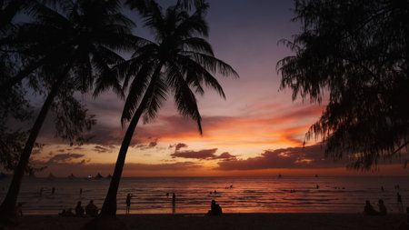 Silhouetted people and palms near sea. Sunset at tropical White beach, Boracay island, Philippines