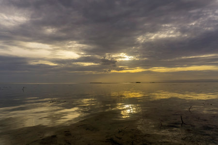 Sunset over calm waters creates a serene atmosphere with golden reflections and dramatic clouds
