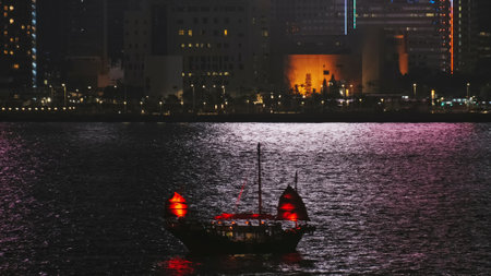 Traditional Chinese Junkboat with red sails sailing in Victoria Harbor at night, Hong Kong
