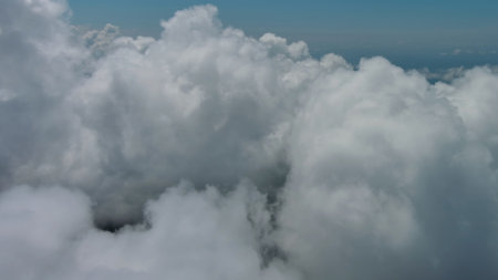Flying through beautiful white fluffy clouds in sky over blue sea. Airplane travel backgroundの写真素材